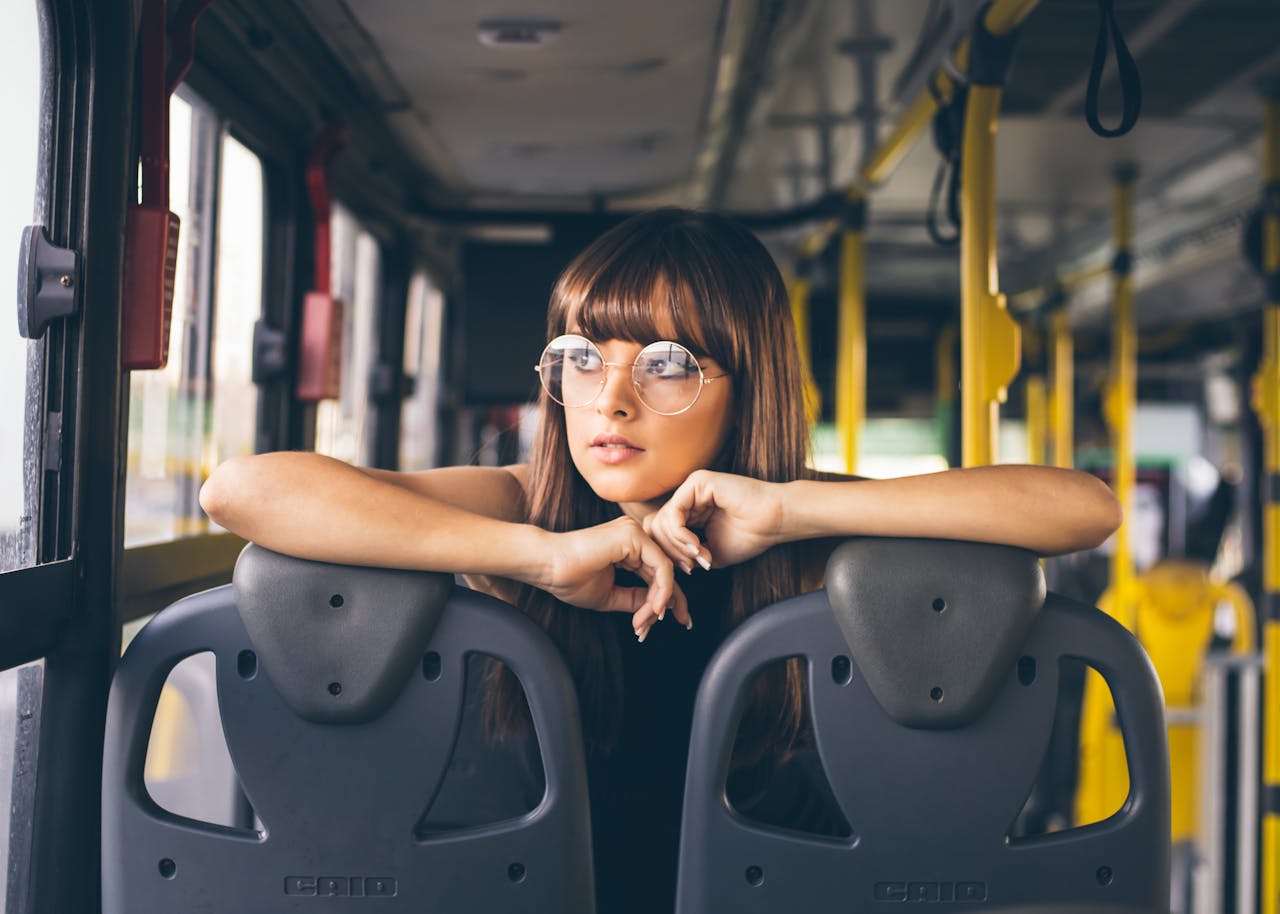 Stylish young woman with glasses poses inside a bus, showcasing fashion and travel style.